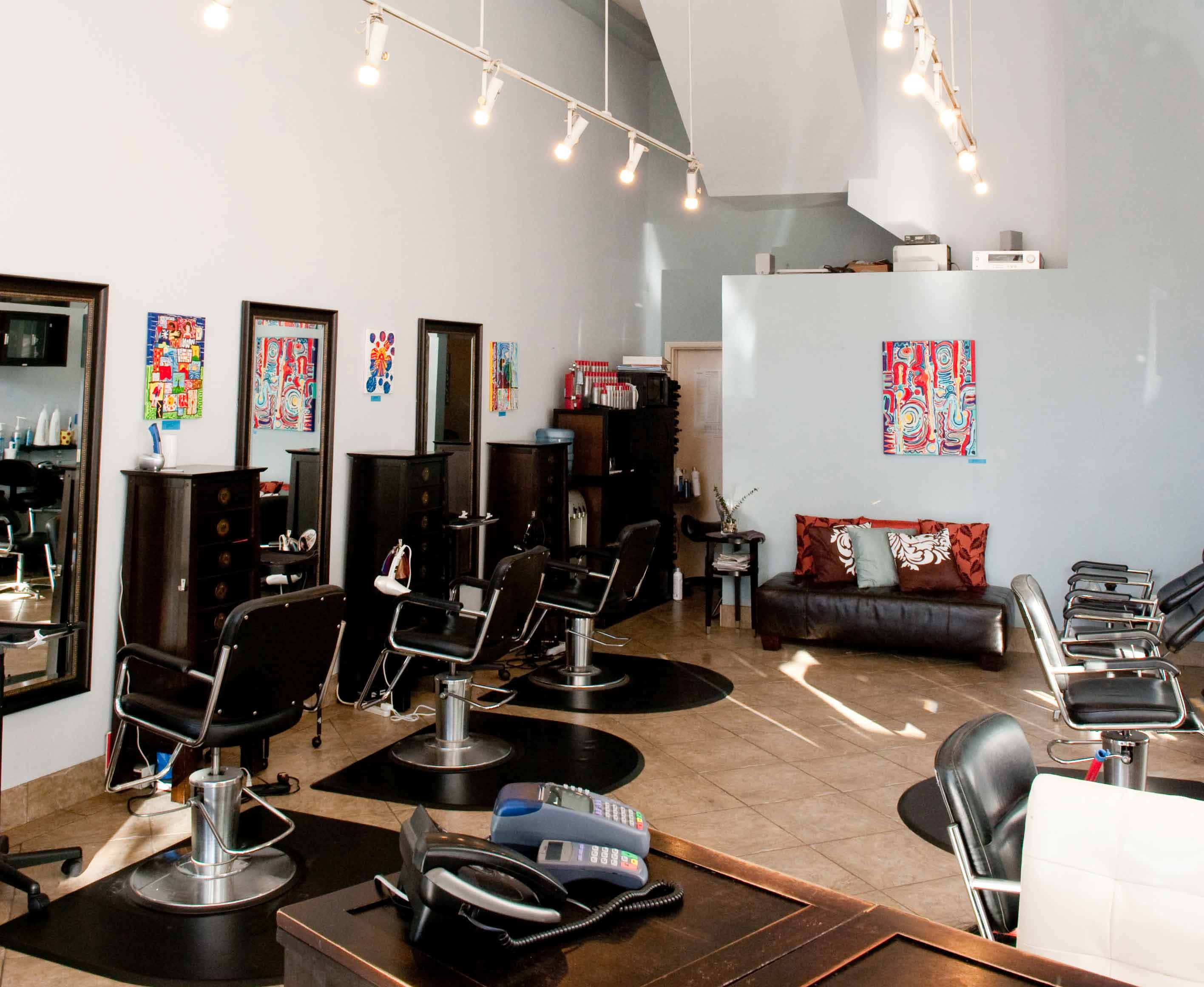 Beauty Salon 桌布 壁紙 — 現代髮廊，配有黑色造型椅、鏡子、色彩繽紛的抽象藝術品和明亮的頭頂燈光。