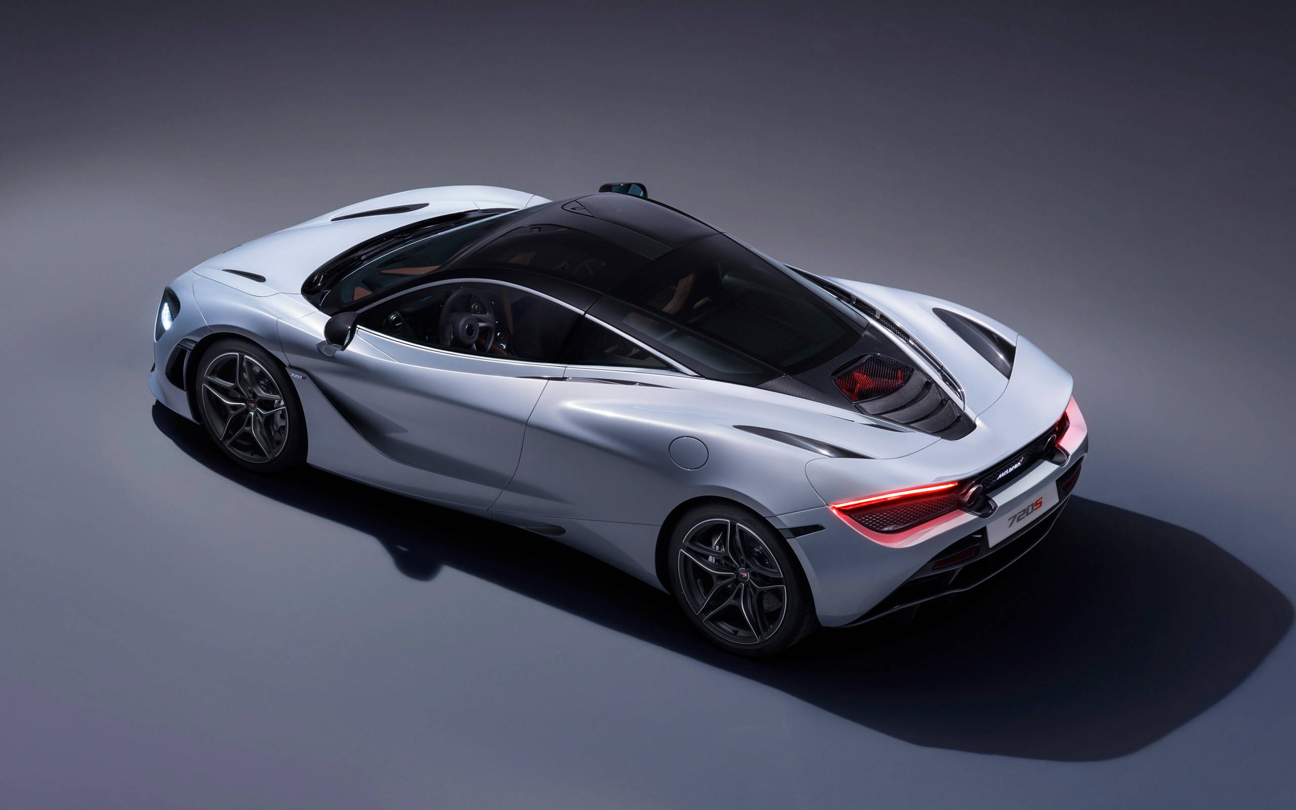 現代麥拉倫720s 4K 壁紙 — 一架時尚的銀色McLaren 720S跑車從高角度拍攝，背景為深灰色攝影棚，燈光效果戲劇化。