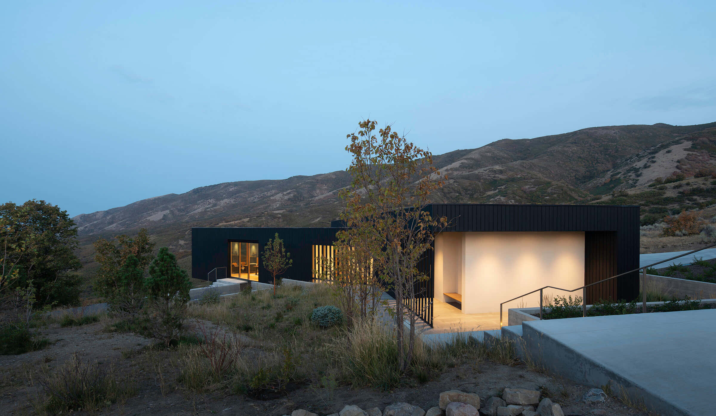 Minimalist Architecture 桌布 壁紙 — 現代黑色房屋，室內溫暖燈光，坐落於暮色中的乾燥山丘。