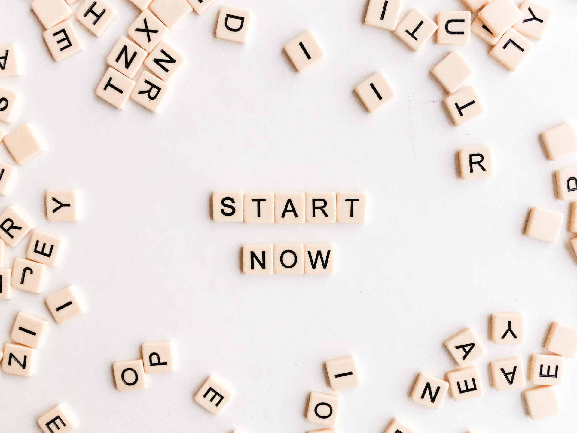 米色字母瓷磚在白色表面上拼出 start now，周圍有散落的字母。