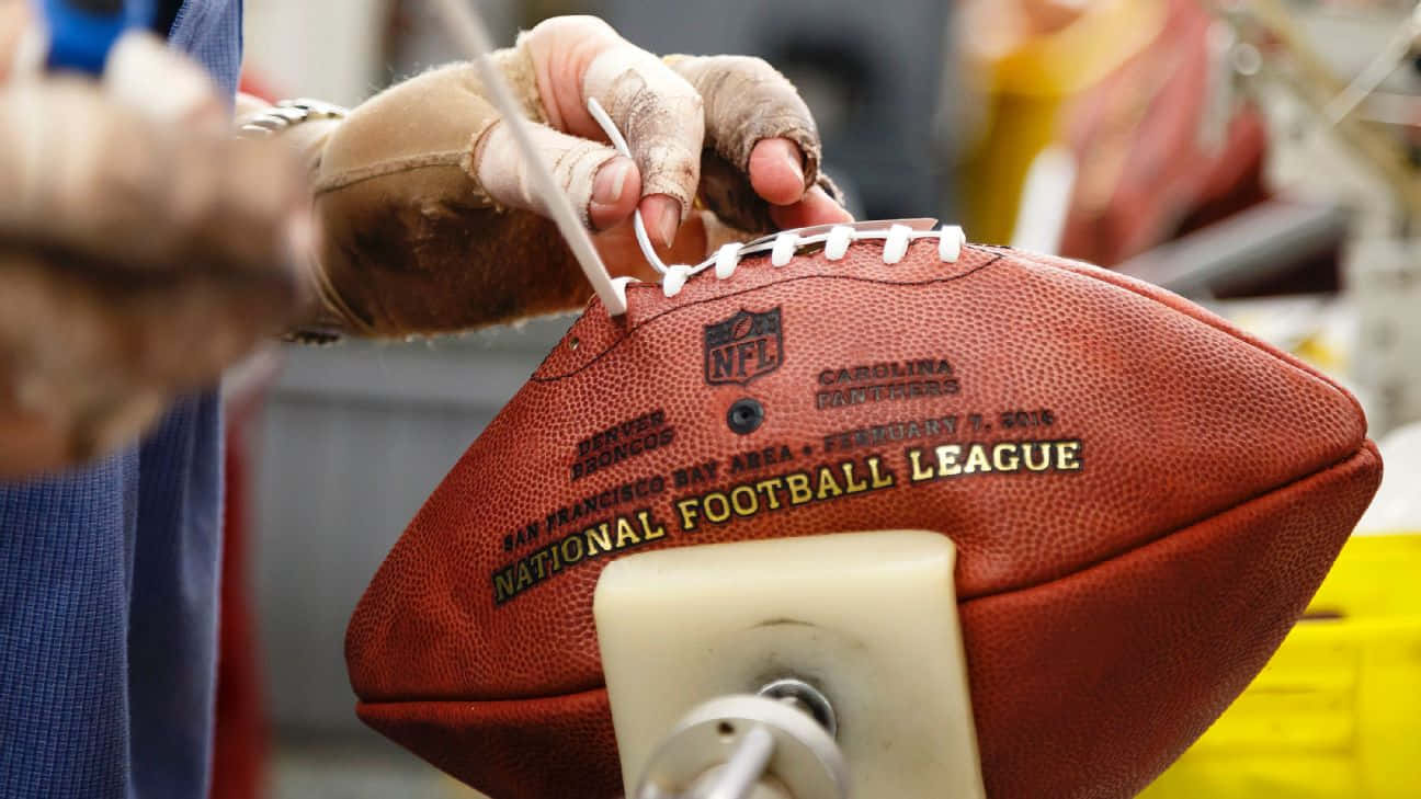 戴手套的手在工場中將鞋帶縫到一個棕色的NFL橄欖球上。