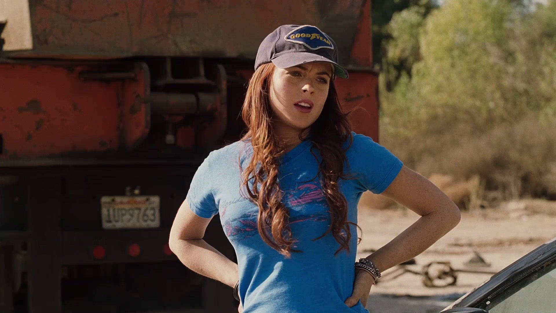 琳賽·蘿涵與Herbie在《Herbie Fully Loaded》中 壁紙 — 一位長紅髮、身穿藍色襯衫和帽子的女性自信地站在一輛生鏽的卡車旁，身處塵土飛揚的戶外環境。