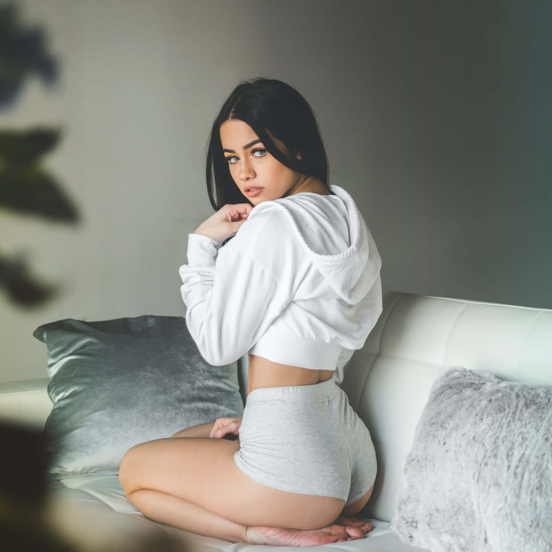 身穿白色連帽衫的女性坐在白色沙發上，配有灰色枕頭
