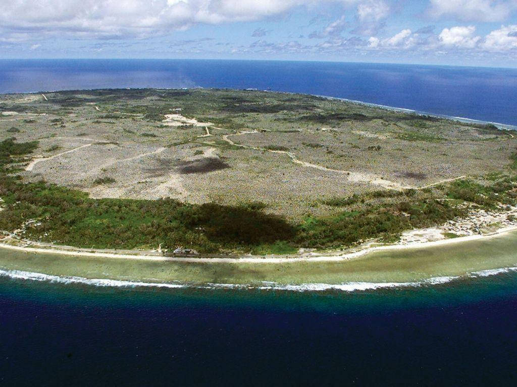 瑙魯島鳥瞰景觀 壁紙 — 一個小型熱帶島嶼的鳥瞰圖，擁有沙灘、珊瑚礁和稀疏植被，被深藍色海洋環繞。