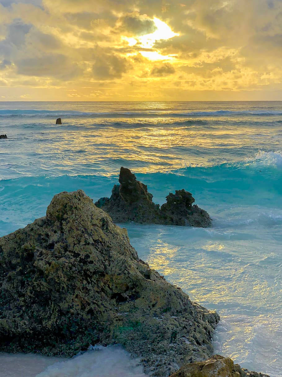 瑙魯海浪拍打珊瑚礁 壁紙 — 金色夕陽照耀在碧綠色的海浪上，拍打著崎嶇的海岸岩石。