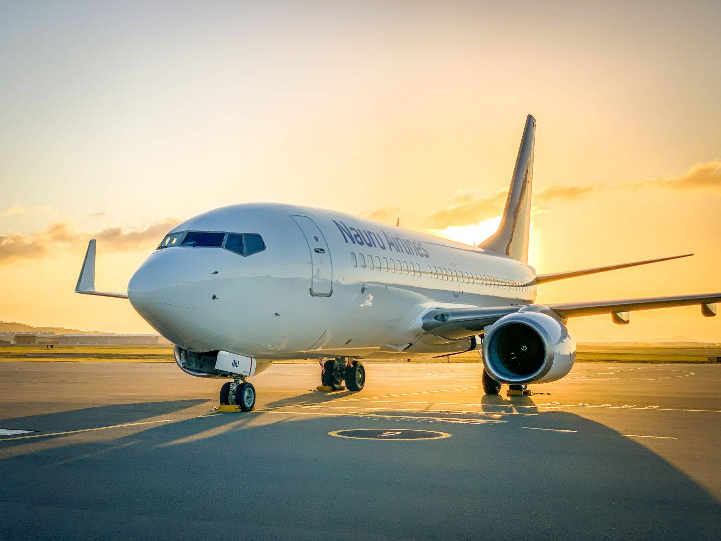 瑙魯航空公司的飛機停泊於跑道 壁紙 — 一架瑙魯航空客機停在機場停機坪上，沐浴在金色的夕陽中，投下長長的影子。