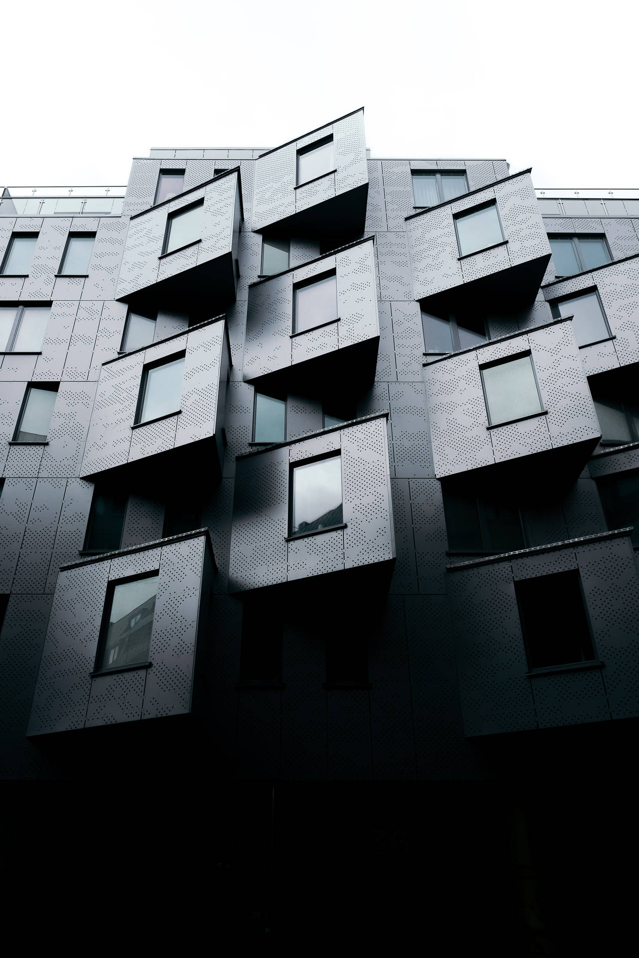 現代建築，帶有突出的陽台和穿孔面板，在陰天天空下