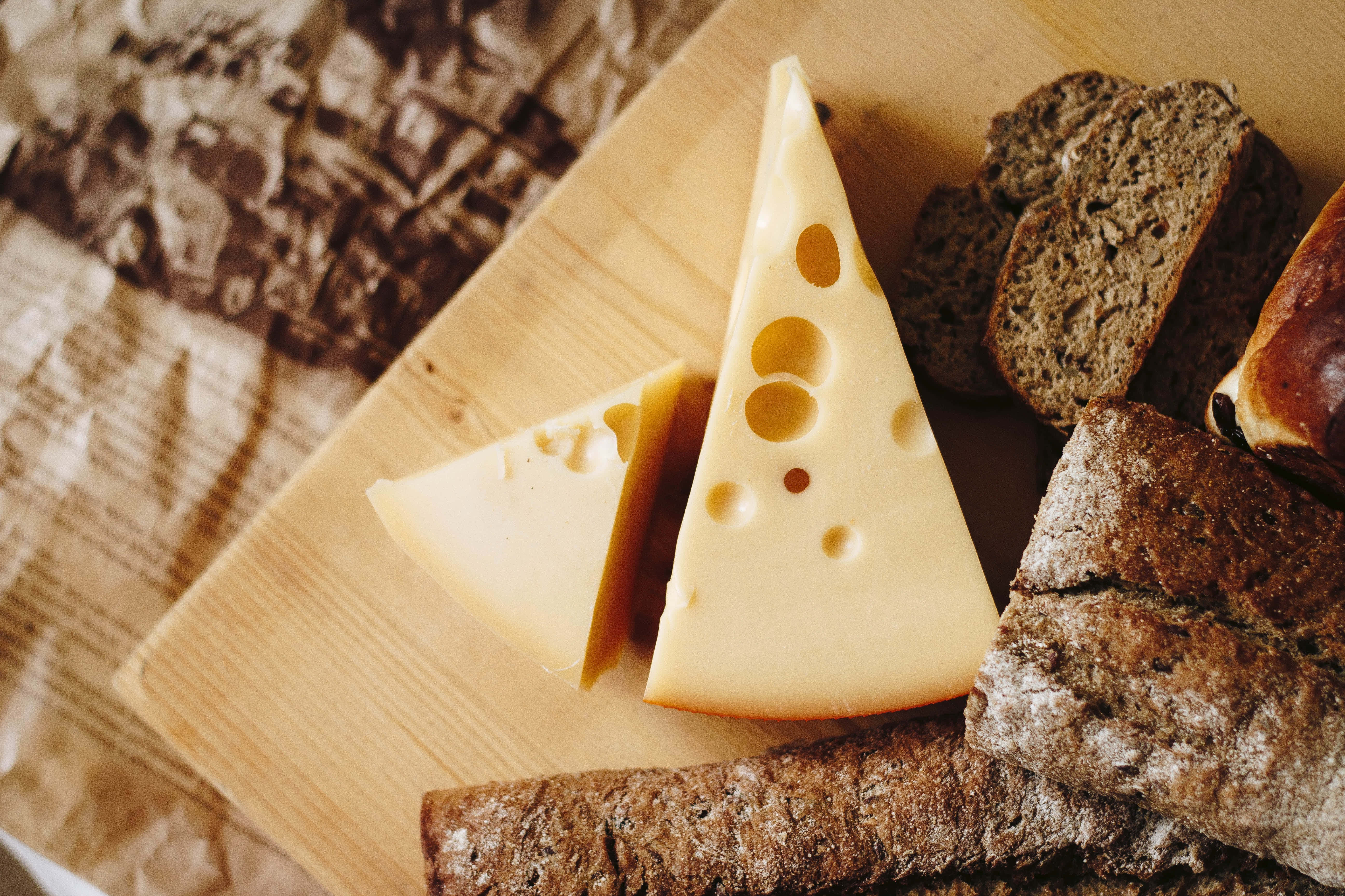 Cheese 桌布 壁紙 — 瑞士芝士（有孔）與鄉村黑麵包的特寫，擺放在木板上，底下是皺巴巴的棕色紙。