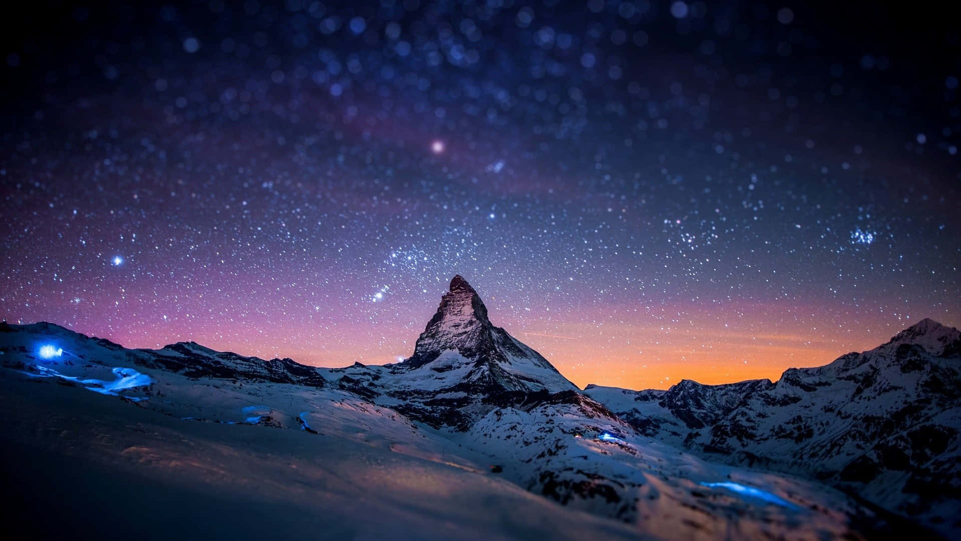 白雪覆蓋嘅山峰喺繁星點點嘅暮色天空下，下面有閃爍嘅光。