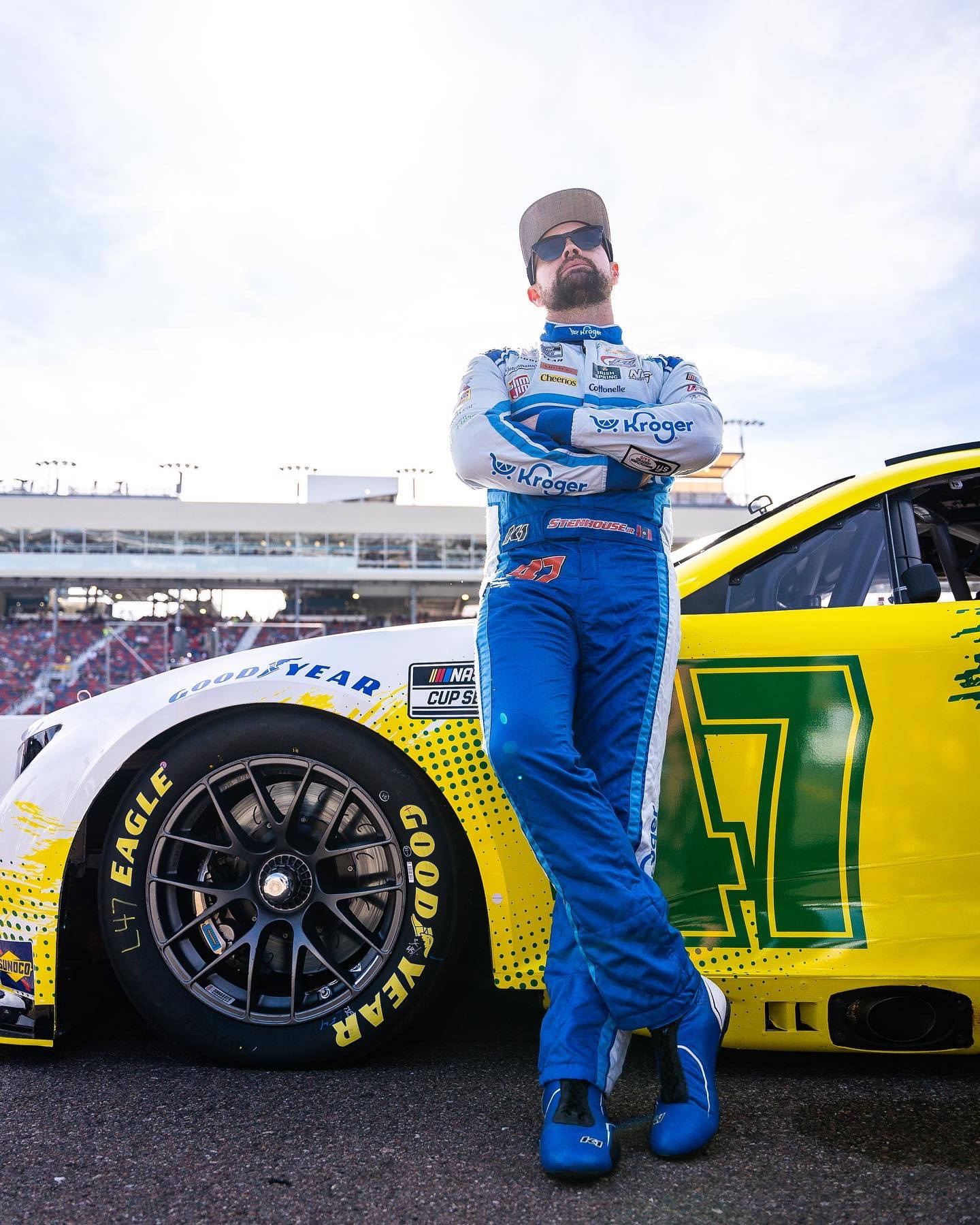 身穿藍色賽車服的NASCAR車手在賽道上靠著黃色賽車。