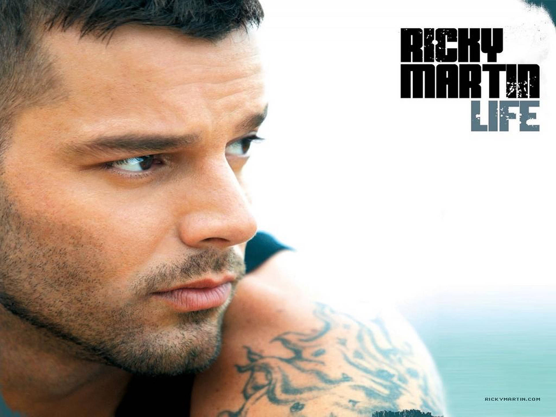 瑞奇·馬丁生命特寫 壁紙 — Ricky Martin 嘅特寫肖像，佢有紋身嘅肩膀，喺明亮模糊嘅背景下沉思咁凝視。