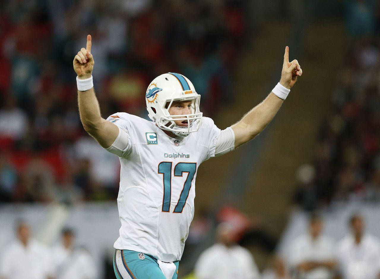 瑞安·坦尼爾NFL比賽中指向上方 壁紙 — 邁阿密海豚隊四分衛17號在夜間比賽中高舉雙食指慶祝勝利。