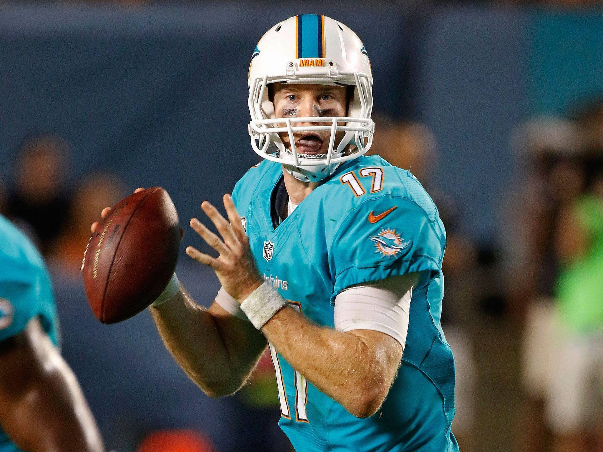 瑞安·坦尼爾NFL比賽隨拍 壁紙 — 一名身穿青綠色球衣的邁阿密海豚四分衛在夜間比賽中，於球場燈光下準備擲出橄欖球。