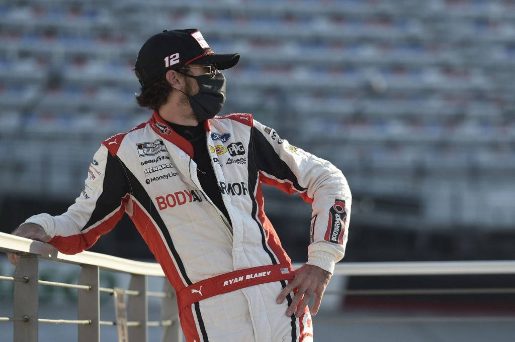 NASCAR車手Ryan Blaney穿著賽車裝備靠在體育場的欄杆上。