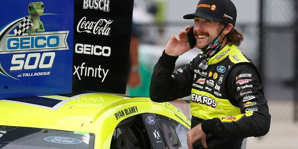 NASCAR車手Ryan Blaney在塔拉迪加他的黃色賽車旁微笑。