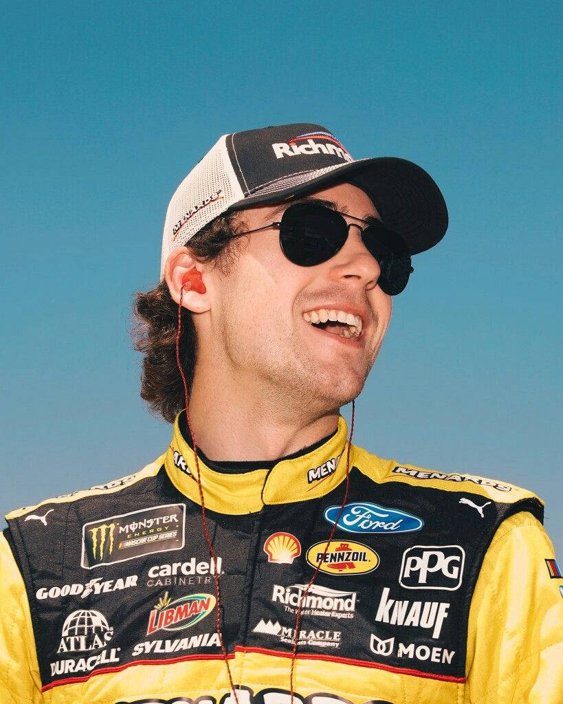 NASCAR車手穿著賽車服微笑，戴著太陽眼鏡和贊助商標誌。