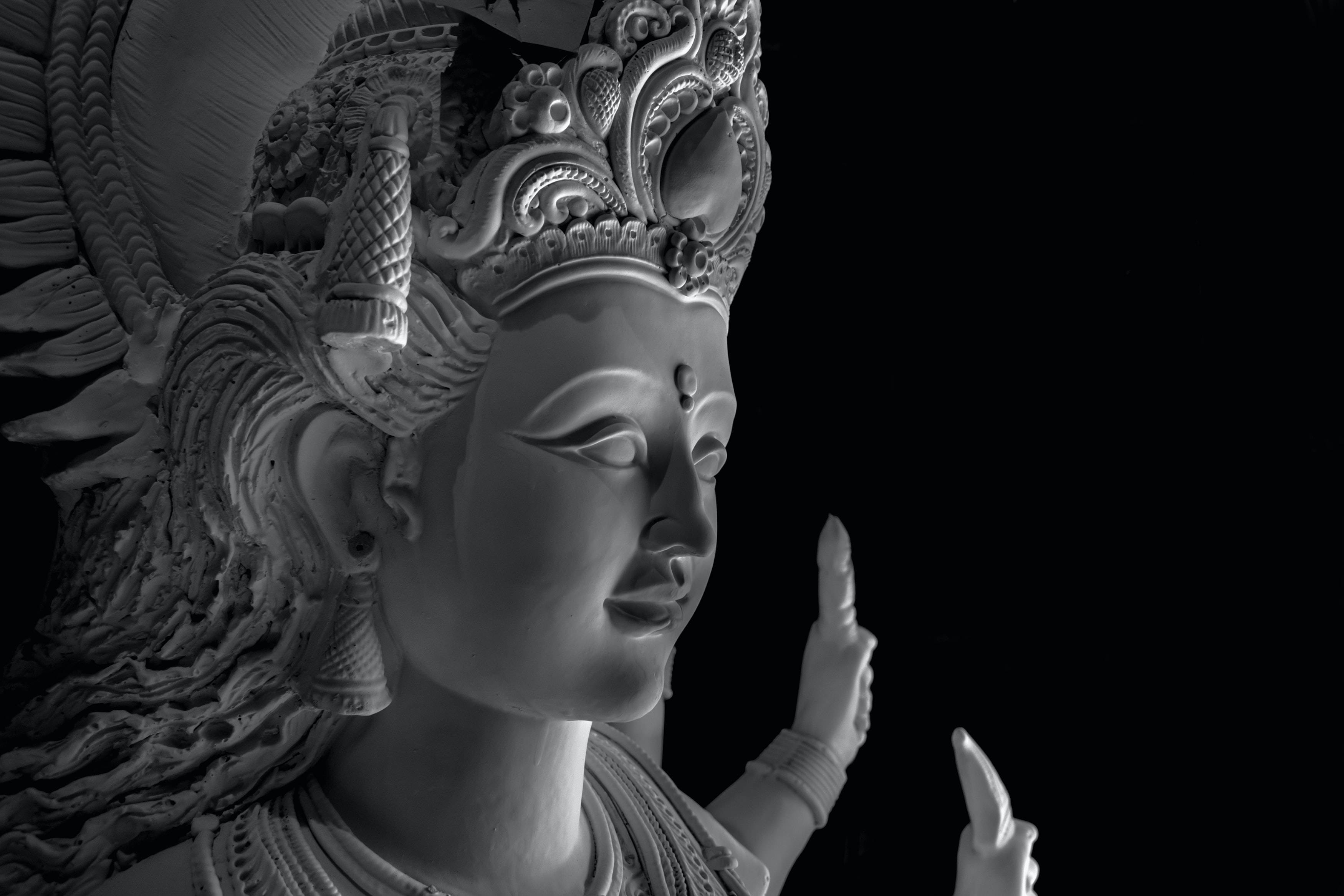 瑪塔拉尼灰色雕像 壁紙 — 一個神聖人物的寧靜單色雕塑，帶有精緻的頭飾和飄逸的頭髮，背景是純黑色。