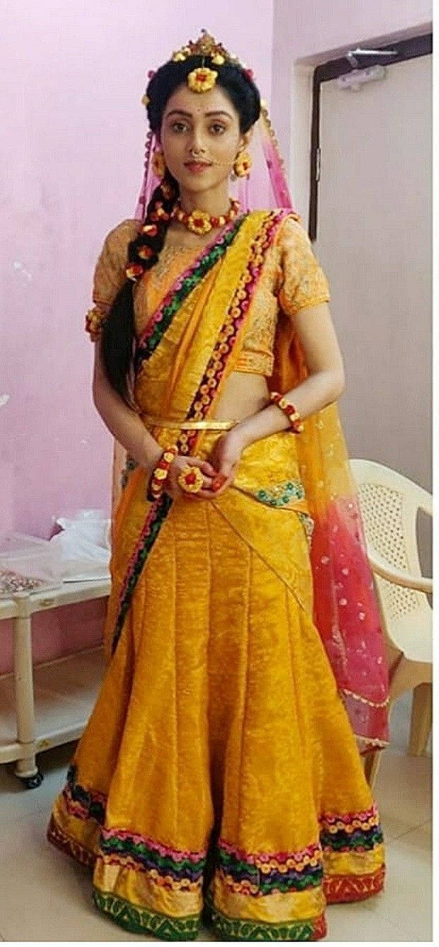 身穿華麗黃色和粉紅色印度 lehenga 並佩戴珠寶的女性，室內。