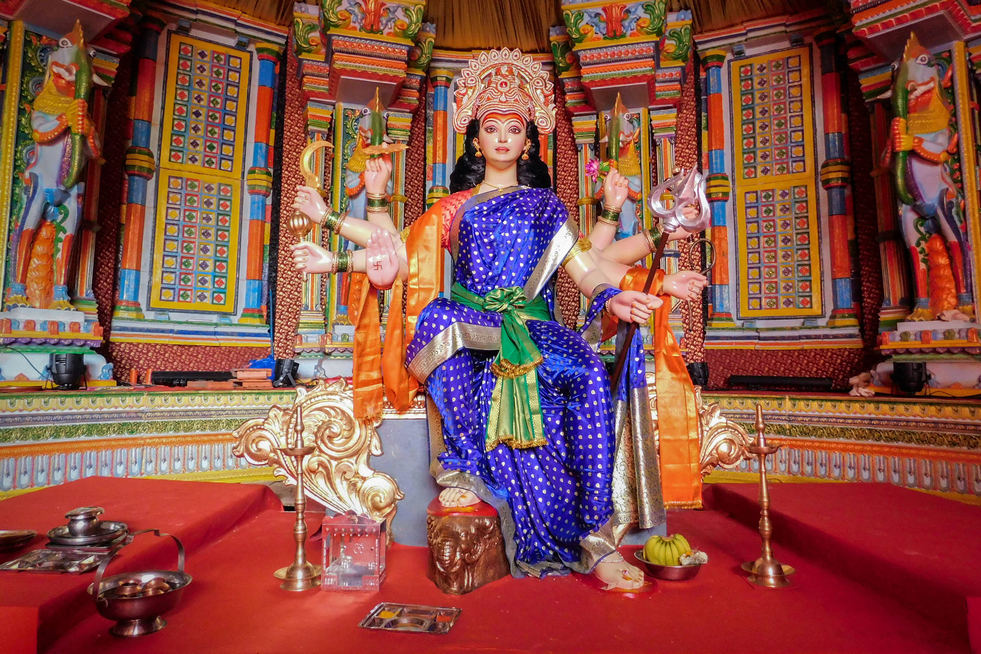一座色彩繽紛的印度教女神雕像，坐在裝飾寺廟內的紅色平台上。