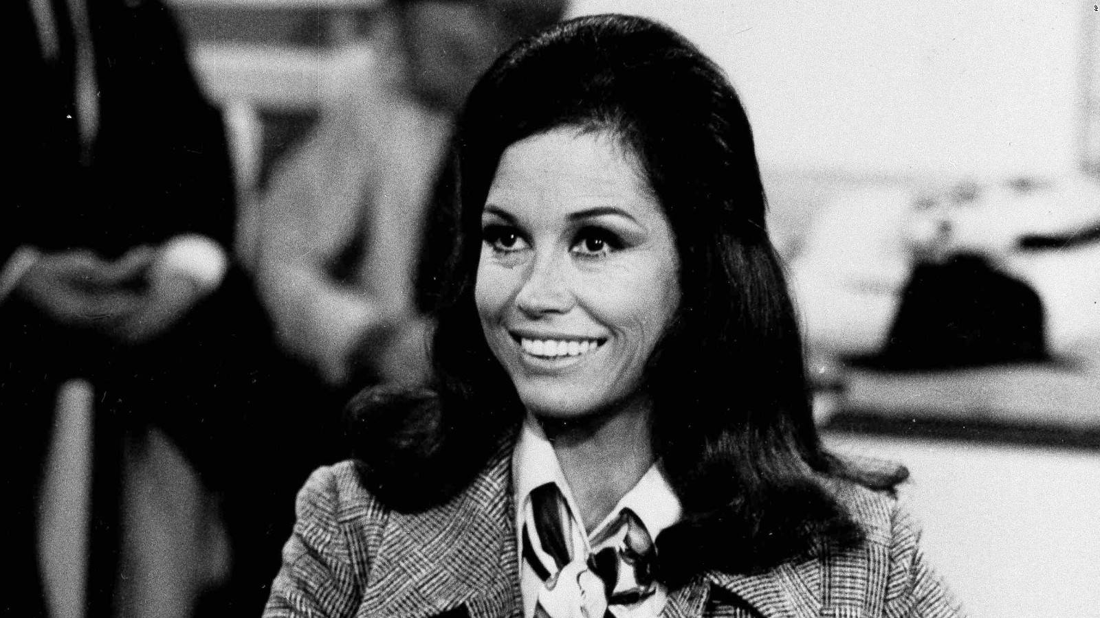 穿著1970年代西裝外套的女性在黑白工作室肖像中微笑。