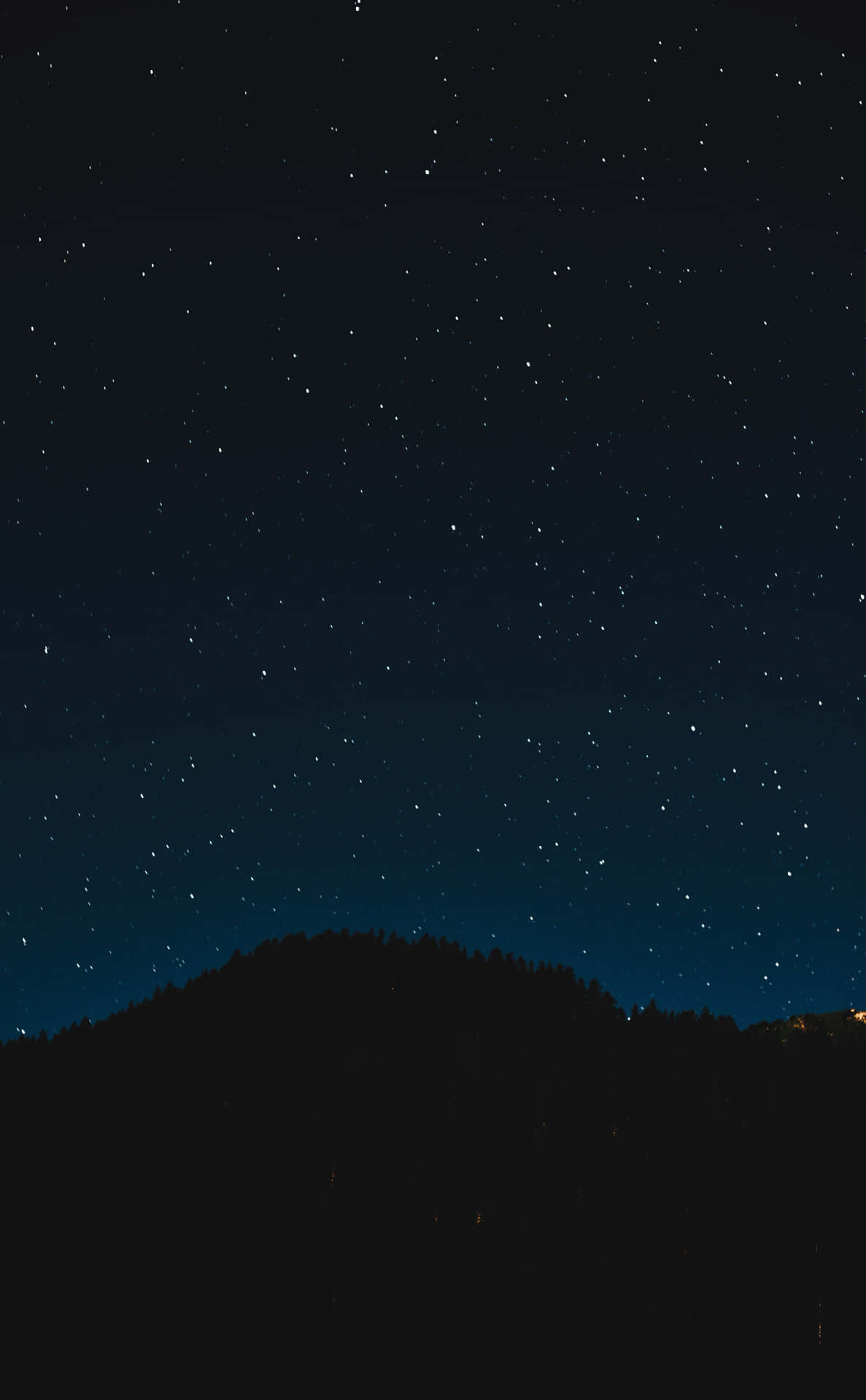 黑暗森林山丘上方的星空夜空與遠方燈光。