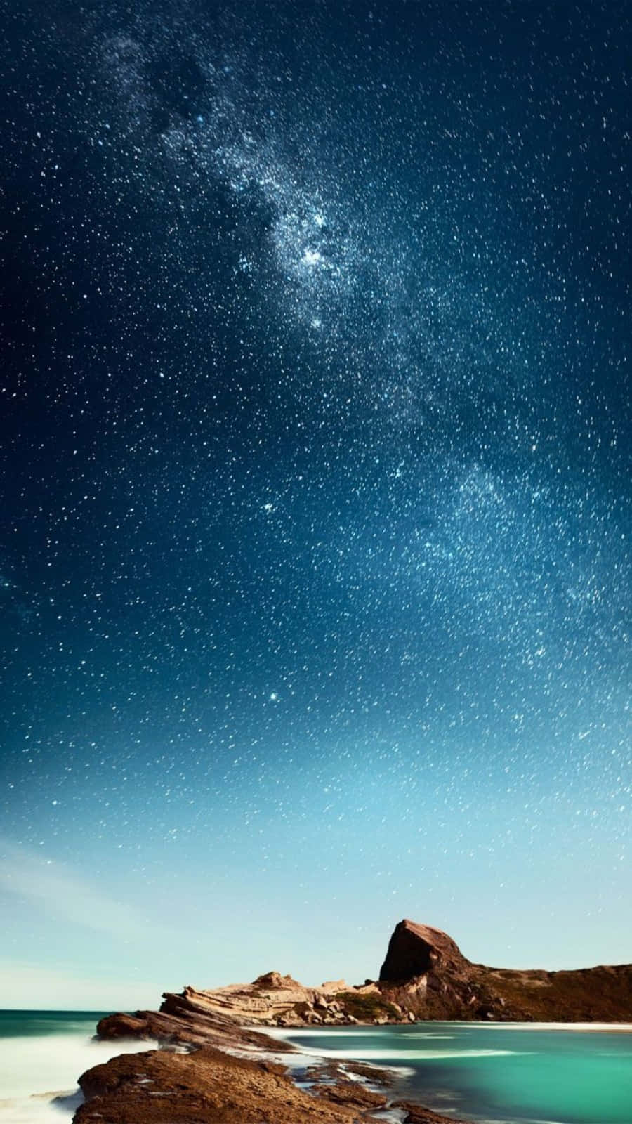 銀河系在夜間照耀著岩石海岸線，平靜的碧綠海水。