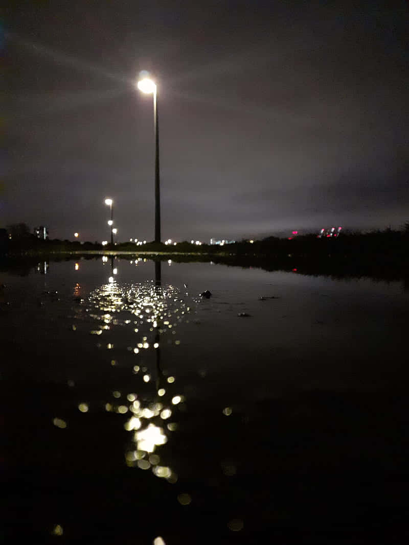 夜晚，路燈在黑暗的天空下倒映在水面上。
