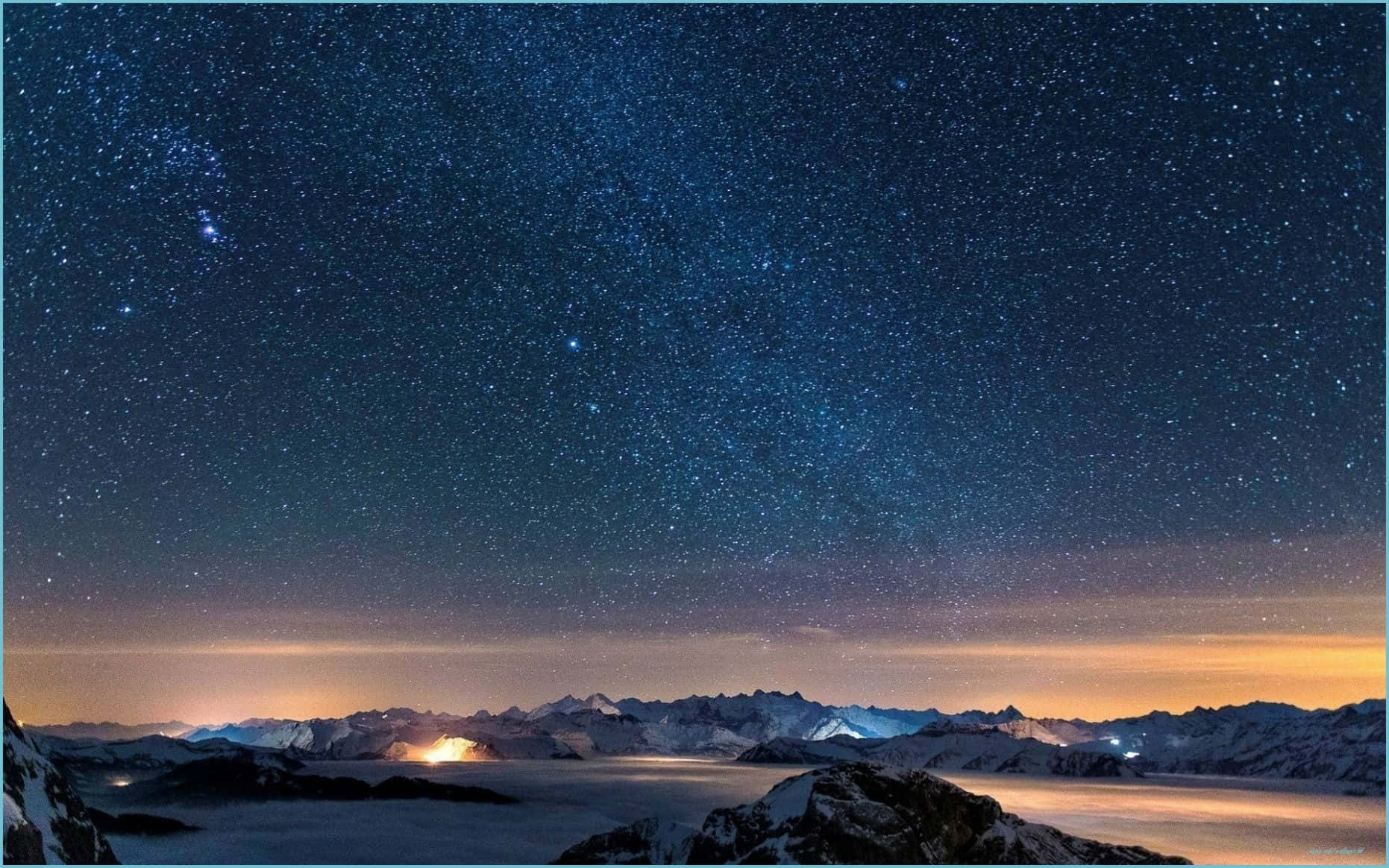 在繁星點點的夜空下，白雪覆蓋的山脈伴隨著極光和遠處的光芒。