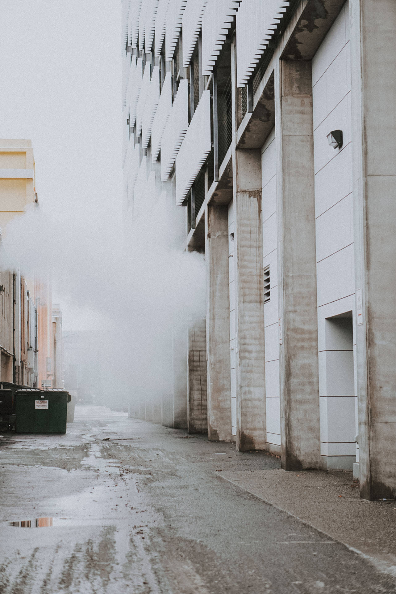 霧氣瀰漫的都市小巷，濕漉漉的路面和現代混凝土建築物。