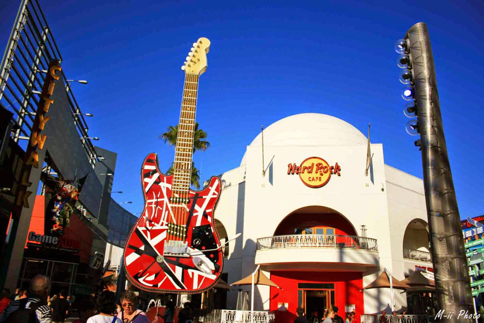 環球影城巨型電吉他 壁紙 — 一個巨大的紅白電結他雕塑聳立在Hard Rock Cafe之上，在晴朗的藍天下，下方聚集了人群。