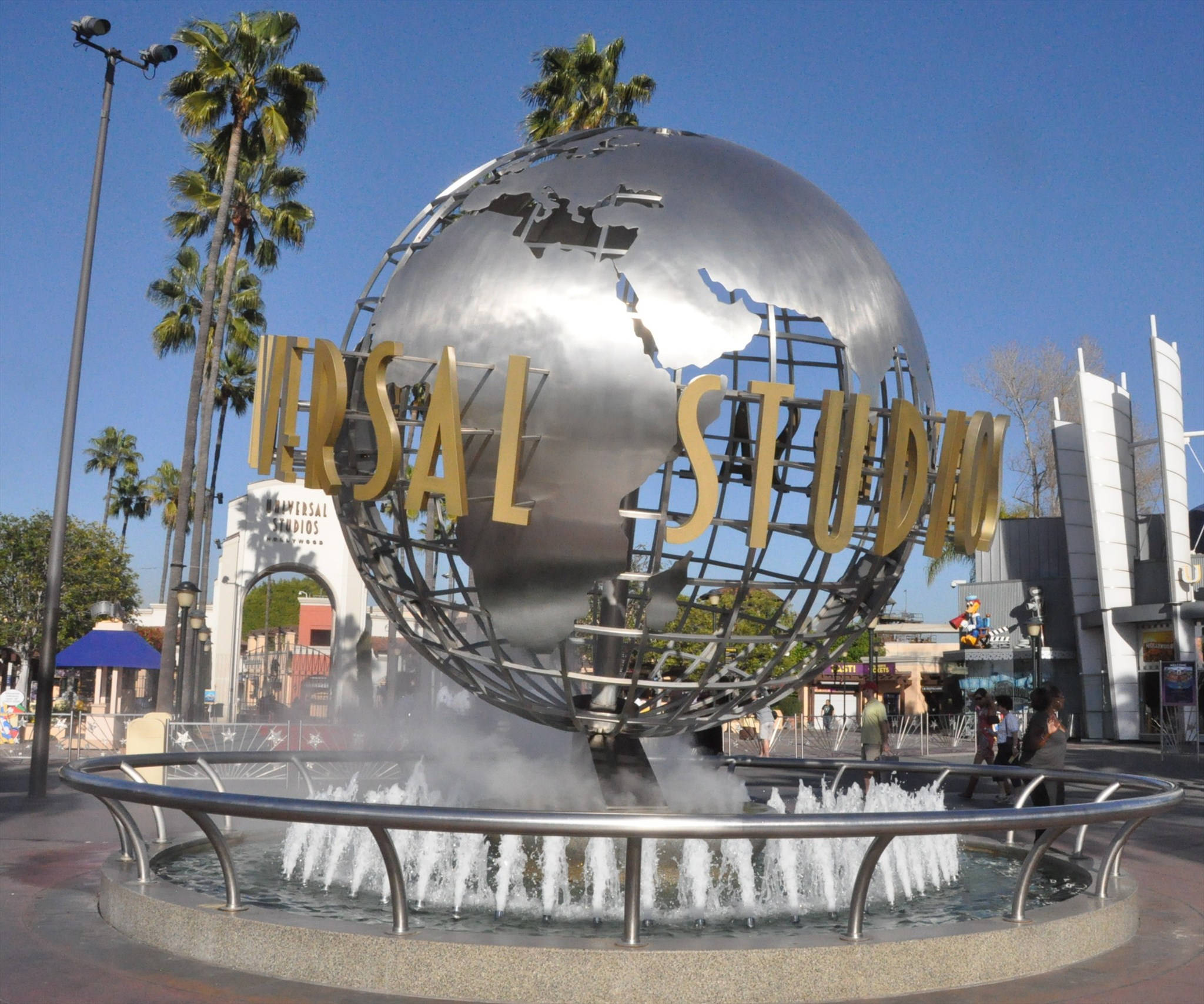 環球影城銀色地球儀 壁紙 — 一個大型金屬地球儀，上面有金色的「Universal Studios」字樣，坐落於噴泉頂部，背景有棕櫚樹和清澈的藍天。