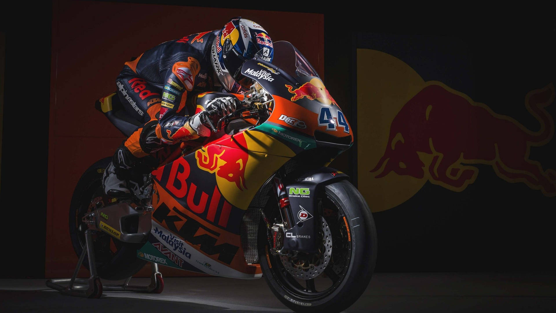 身穿Red Bull KTM裝備的電單車賽車手在工作室內以標誌為背景，在電單車上擺姿勢。 — 賽車 壁紙