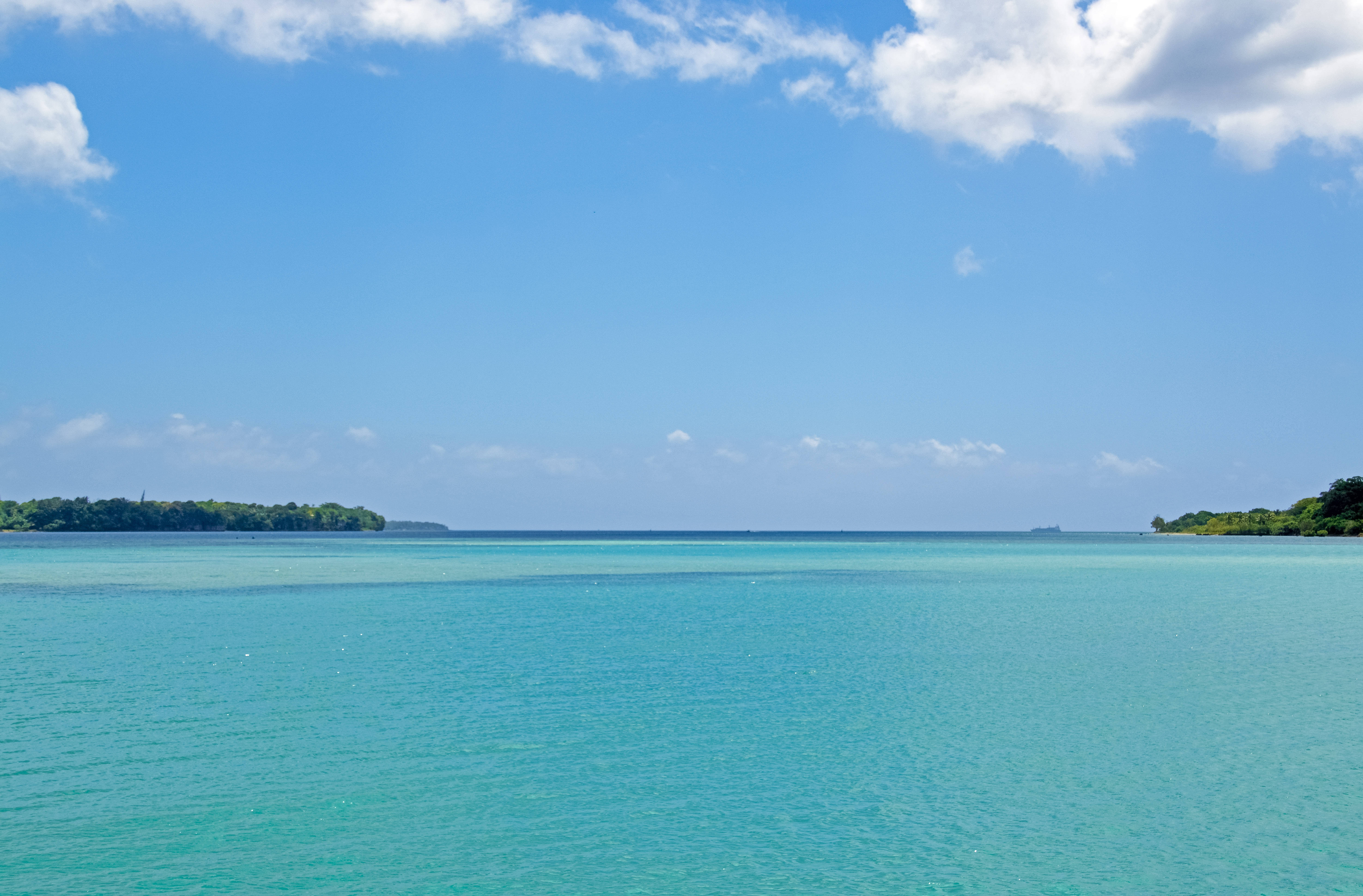 瓦努阿圖埃法特島 壁紙 — 廣闊的藍綠色海洋在明亮的藍天下延伸，散佈著白雲，地平線上有遙遠的綠色島嶼。