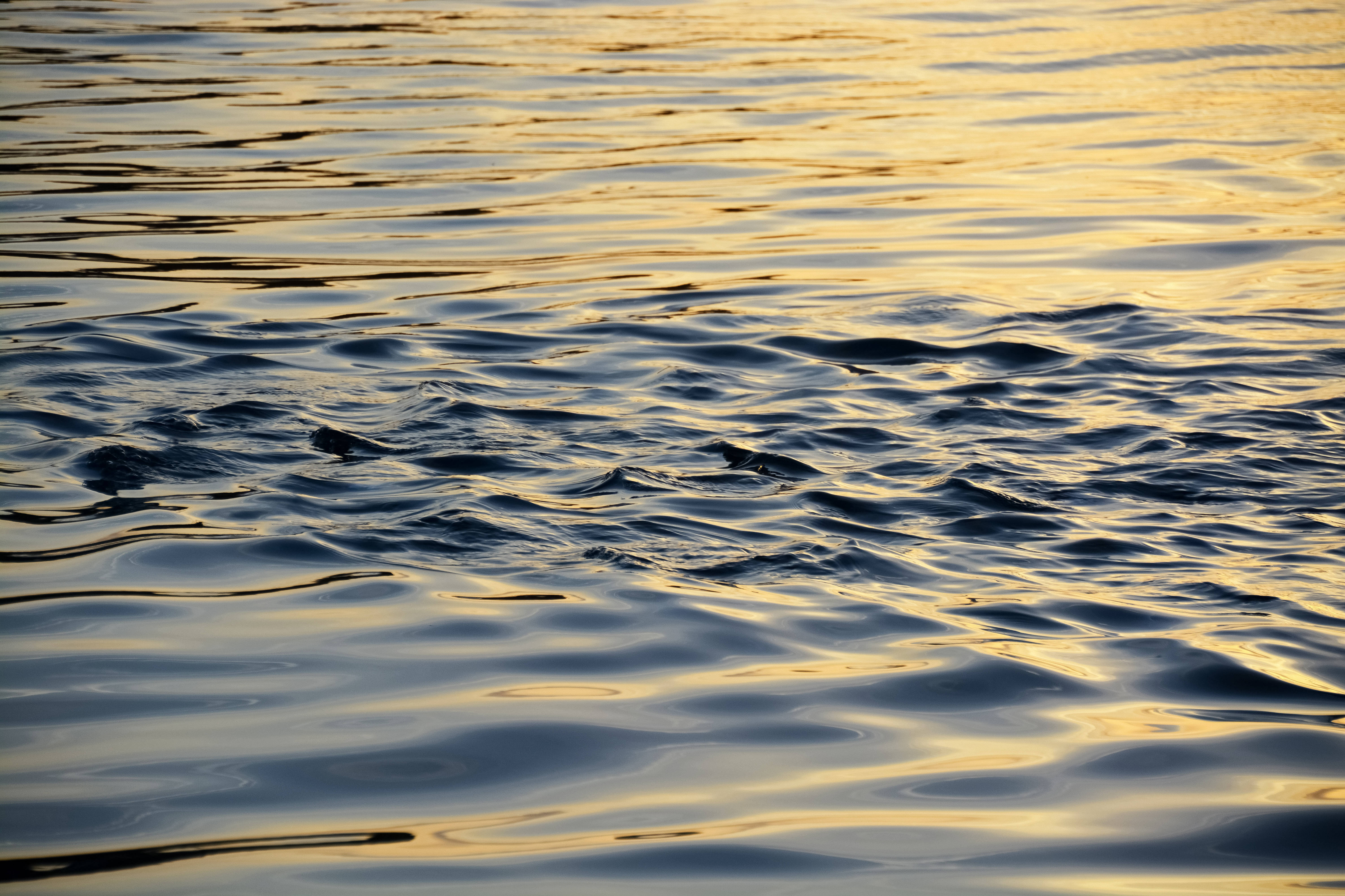瓦努阿圖海浪 壁紙 — 夕陽的光芒在漣漪的水面上閃爍，形成金色和藍色的抽象圖案。