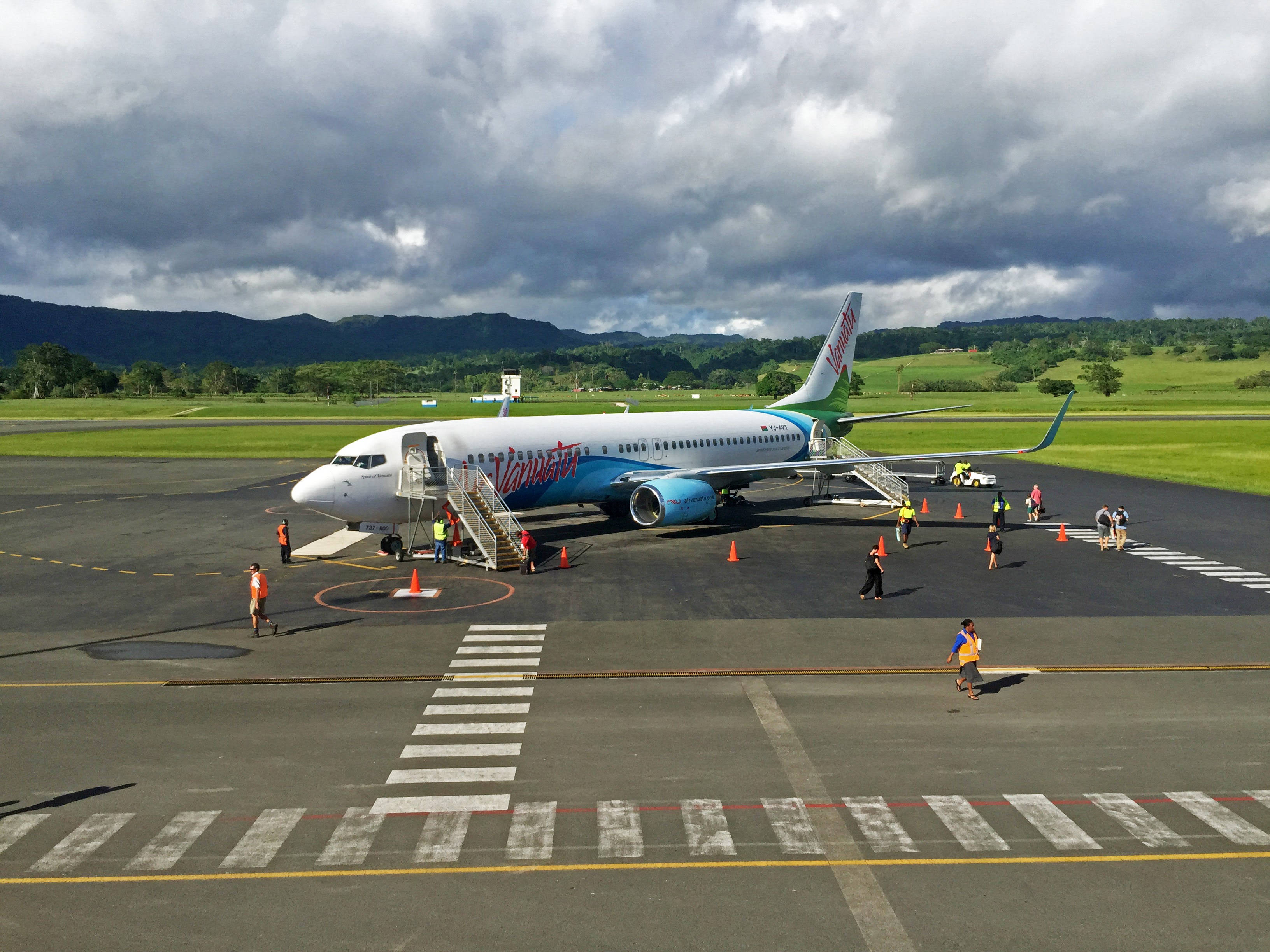 瓦努阿圖飛機 壁紙 — 一架維珍澳洲航空飛機停在停機坪上，背景是戲劇性的暴風雲，附近有地勤人員和乘客。