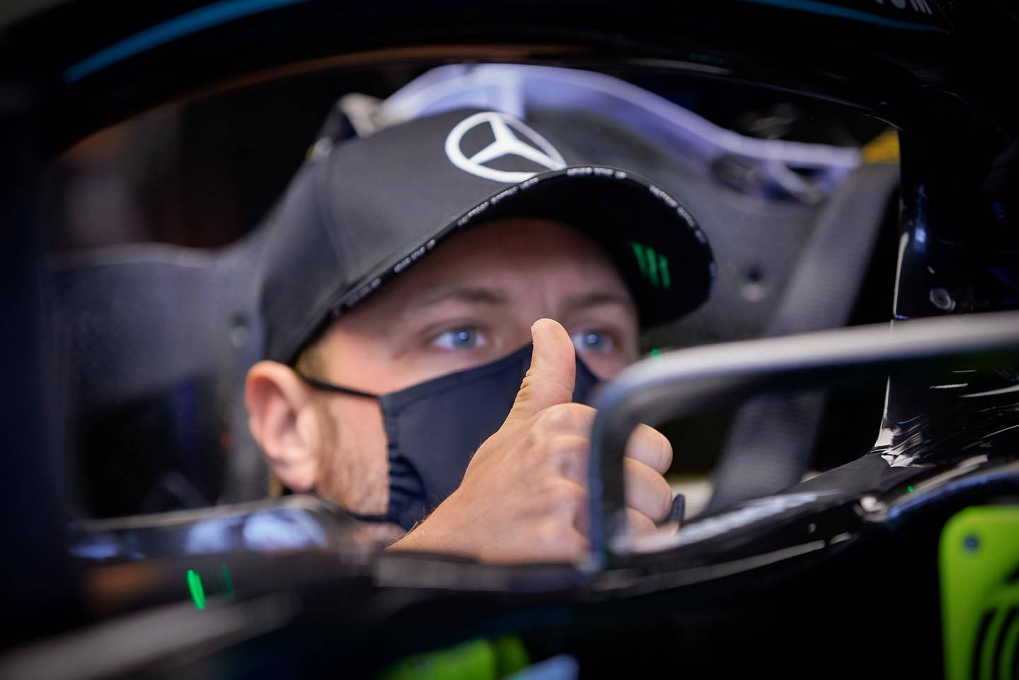 F1車手在賽車駕駛艙內豎起大拇指，戴著口罩和帽子。