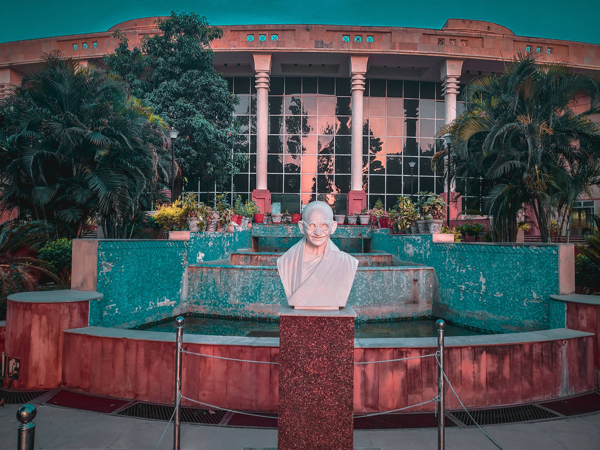 甘地大理石半身像，前面是噴泉和現代建築，周圍有棕櫚樹。