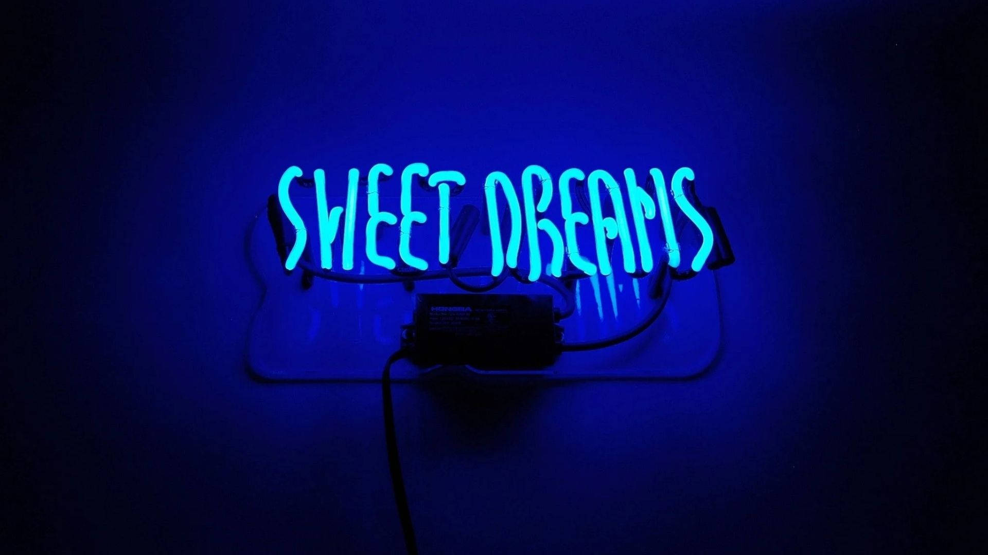 甜夢LED燈光 壁紙 — 一個發光的藍色霓虹燈牌，上面寫著 sweet dreams，在昏暗的房間中將柔和的光線投射在深色牆壁上。