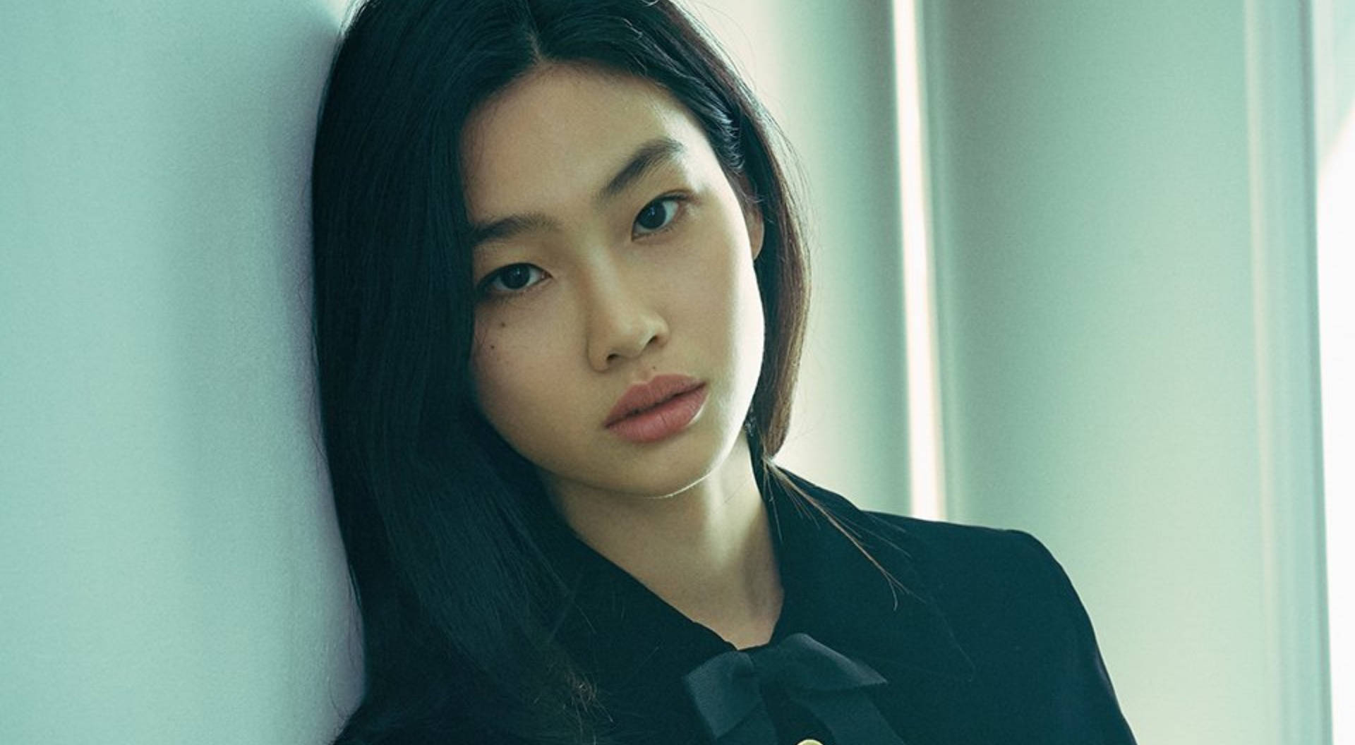 穿黑色上衣的年輕女子在柔和燈光下靠著藍色牆壁。