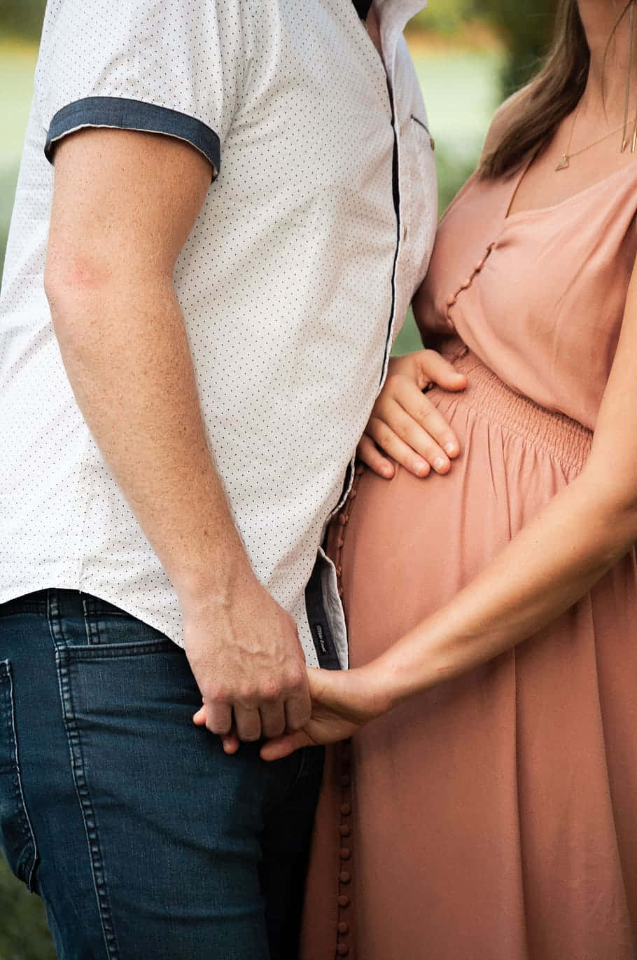 一個男人和一個孕婦在戶外溫馨的時刻手牽手。