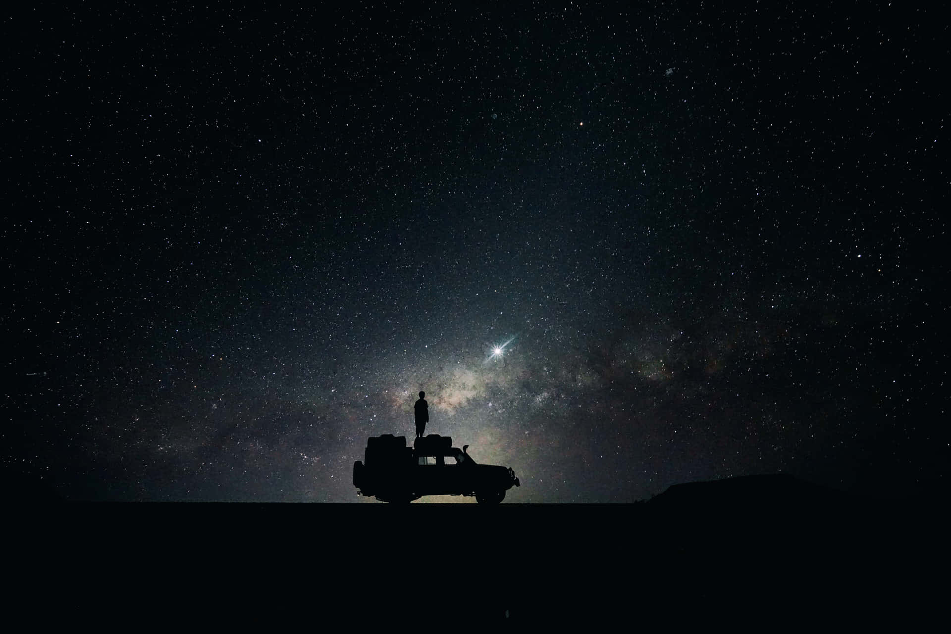 在星空下，SUV上的人影凝視著銀河的剪影