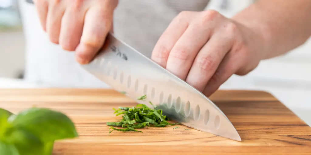 一個人在木砧板上用刀切碎新鮮羅勒。