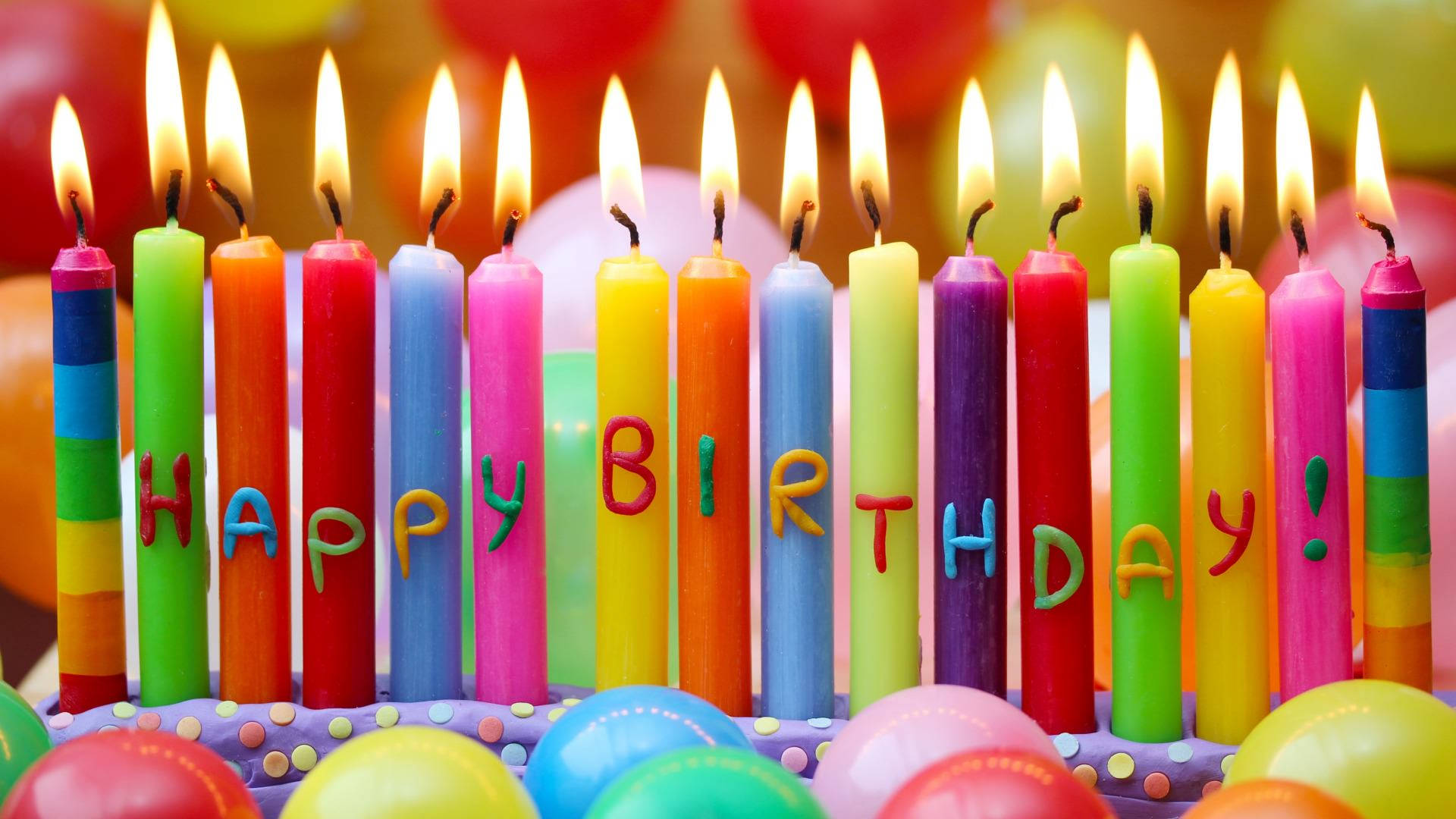 生日快樂彩色蠟燭 壁紙 — 特寫鏡頭：色彩繽紛的生日蠟燭在蛋糕上拼出「生日快樂」，燭火點燃，周圍環繞著氣球。