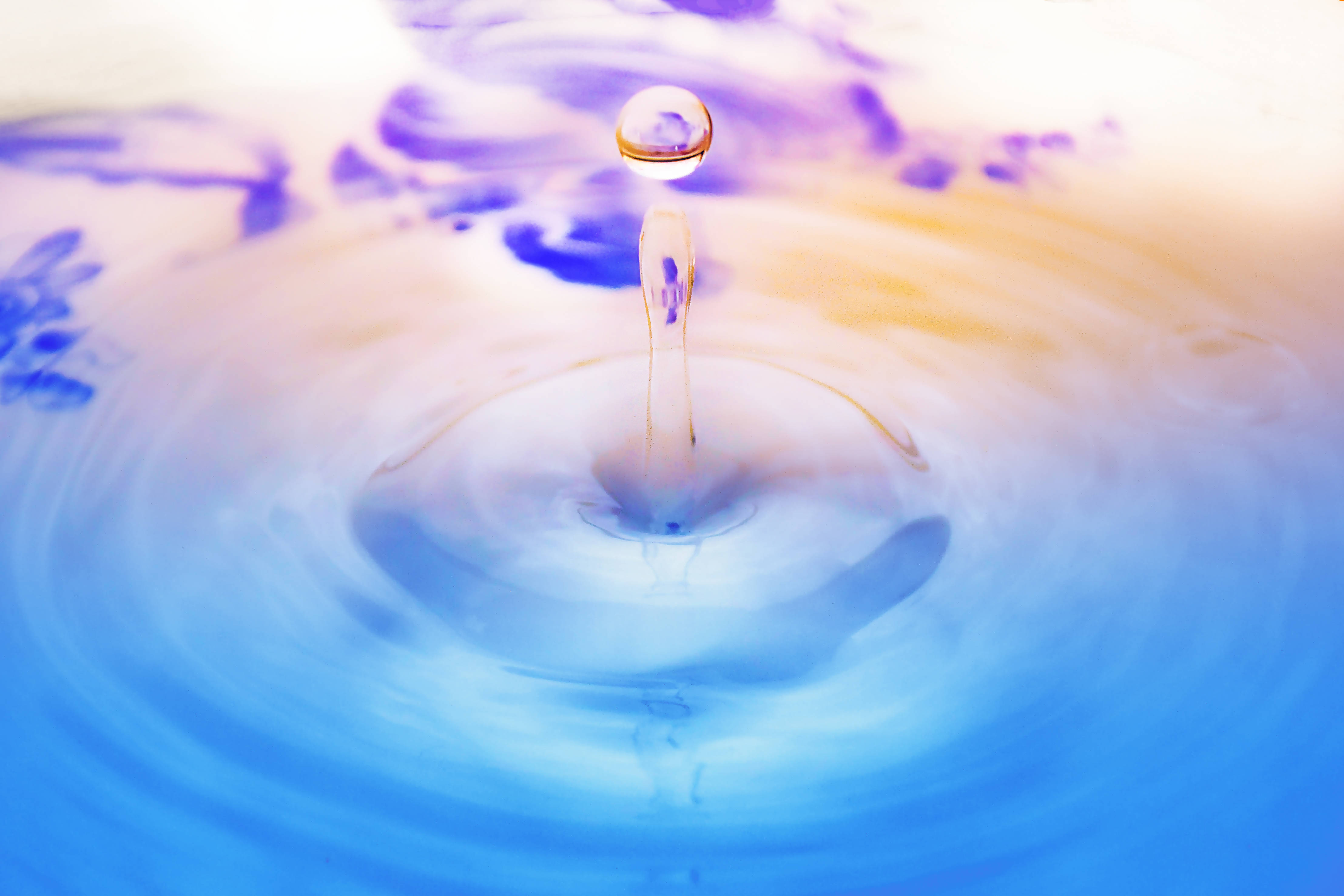 生機盎然的色彩：一滴絢麗水珠 壁紙 — 完美嘅水滴懸浮喺半空中，下面係泛起漣漪嘅藍色同紫色液體池。