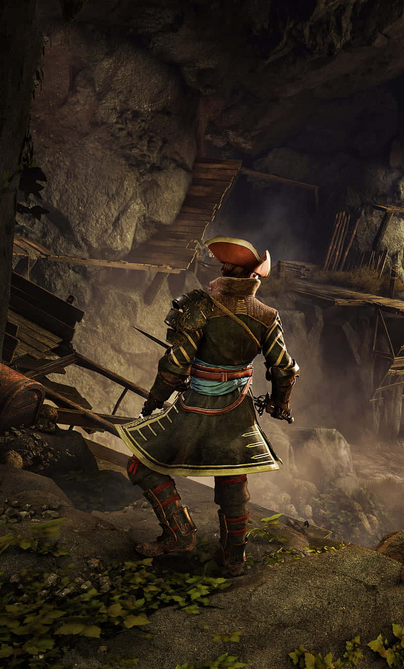 用 Android《Greedfall》探索新世界 壁紙 — 一位身穿華麗盔甲的武士站在岩石峭壁上，俯瞰著一個迷霧籠罩、破敗的木結構建築，該建築坐落在洞穴般的懸崖中。