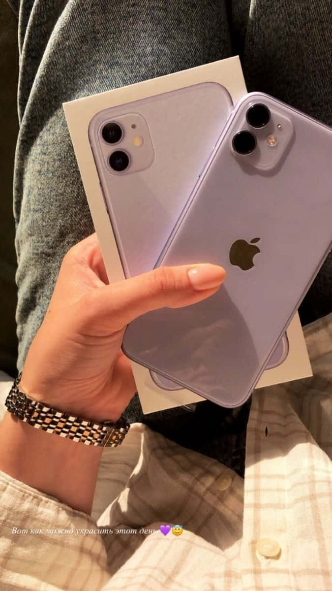 用 iPhone 12 解鎖 5G 的強大效能 壁紙 — 一隻手拿著薰衣草色 iPhone 11 Pro 及其盒子，背景是舒適的格仔襯衫和灰色布料。