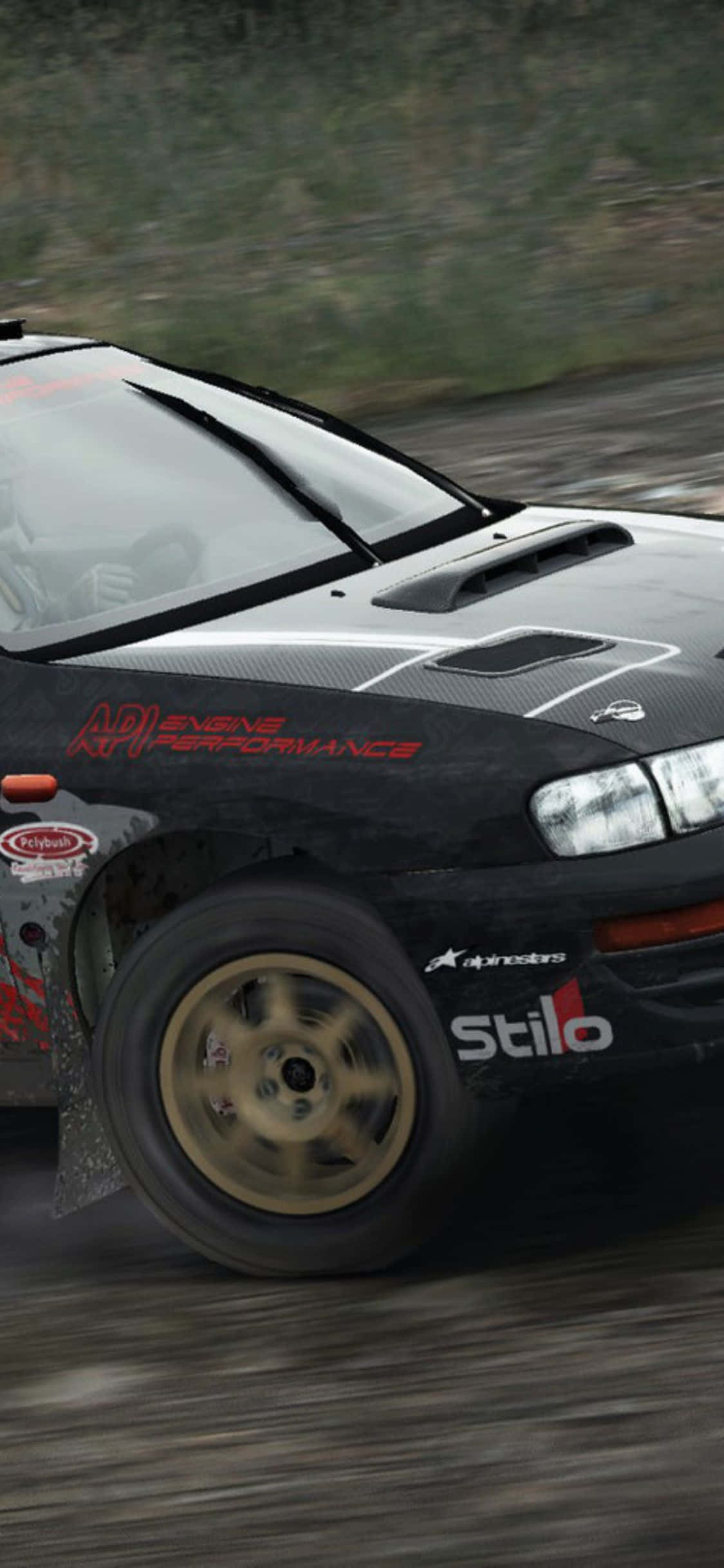 用 iPhone X 和《Dirt Rally》衝向終點 壁紙 — 一輛黑色拉力賽車配金色輪圈，在泥濘的林間小徑上飛馳，濺起泥土和水花。