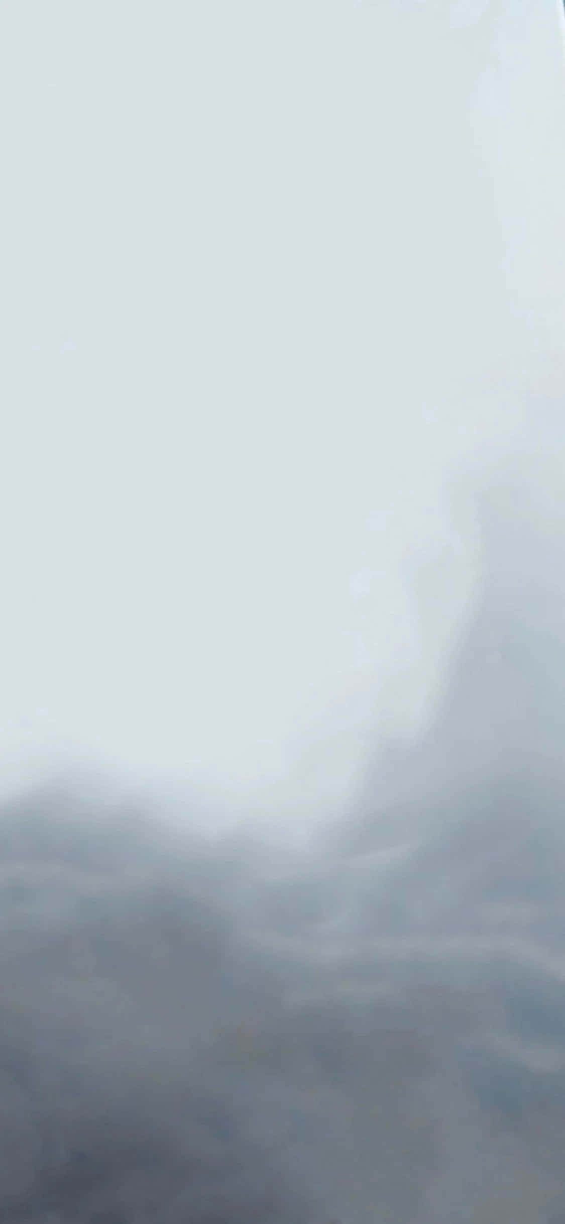 用 iPhone XS 在掌中體驗《死亡擱淺》 壁紙 — 一縷輕柔的薄霧在蒼白的天空中盤旋上升，營造出寧靜的氛圍場景。