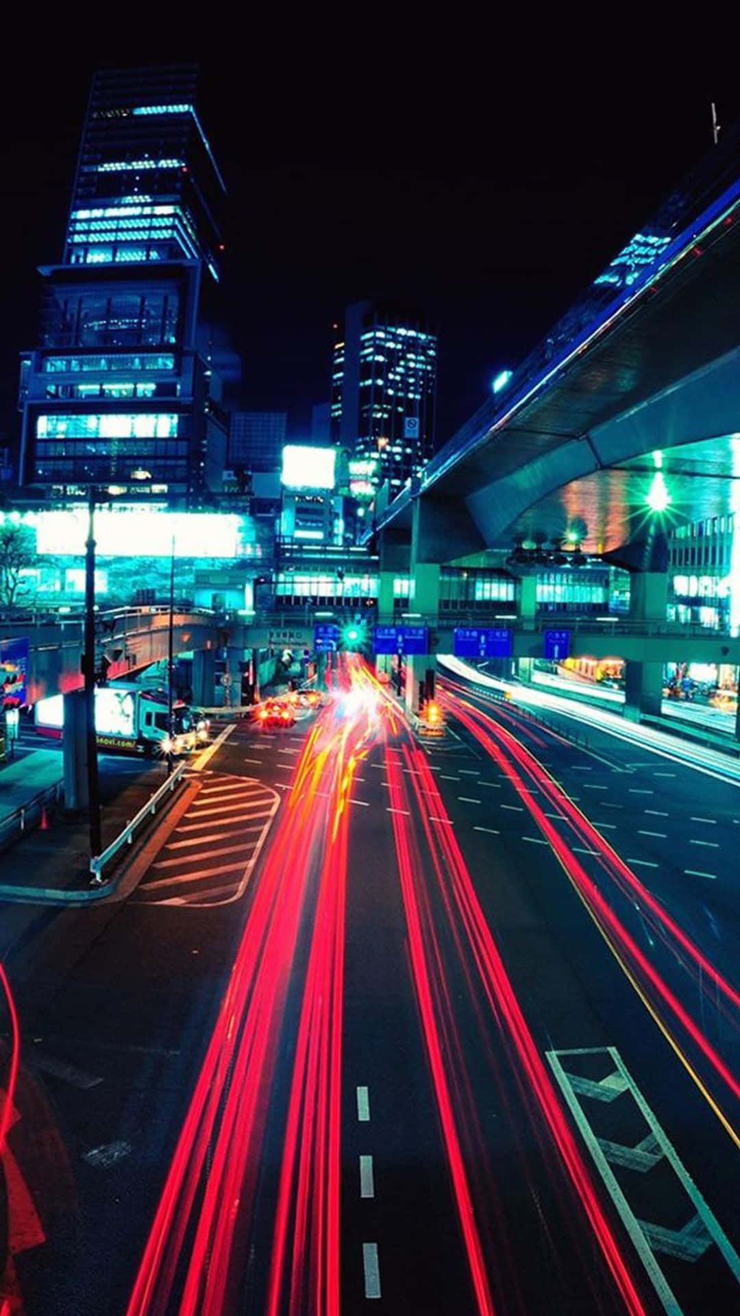 夜間城市街道，帶有紅色車燈軌跡和燈火通明的建築物。