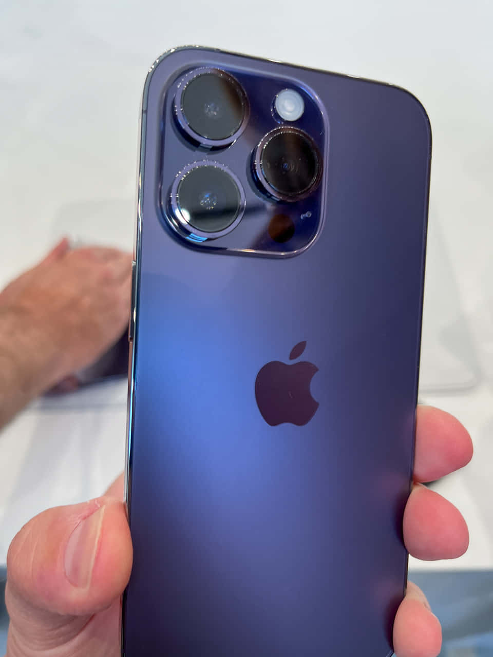 手拿著一部帶有三鏡頭系統的紫色iPhone。